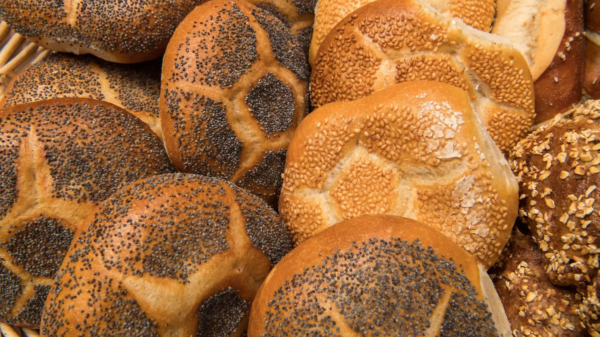 Verschiedene Semmeln liegen in der Auslage einer Bäckerei in einem Korb in der Auslage.