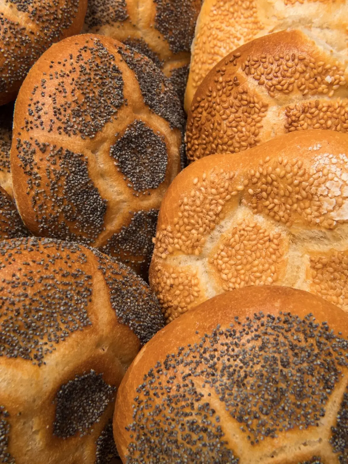 Verschiedene Semmeln liegen in der Auslage einer Bäckerei in einem Korb in der Auslage.