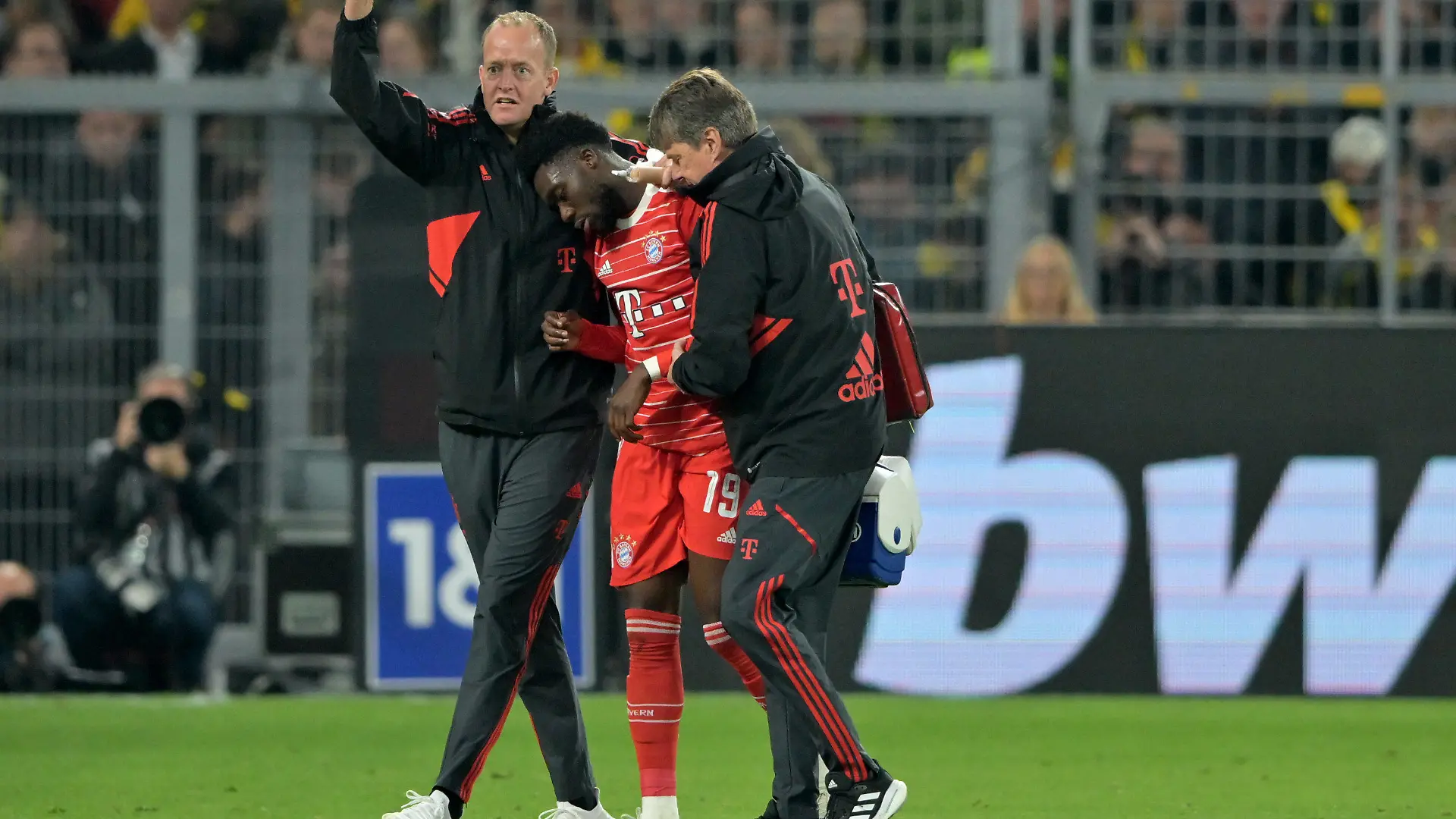 08.10.2022, Nordrhein-Westfalen, Dortmund: Fußball: Bundesliga, Borussia Dortmund - FC Bayern München, 9. Spieltag, Signal Iduna Park. Münchens Alphonso Davies (M) wird nach einer Verletzung vom Platz geführt. WICHTIGER HINWEIS: Gemäß den Vorgaben der DFL Deutsche Fußball Liga bzw. des DFB Deutscher Fußball-Bund ist es untersagt, in dem Stadion und/oder vom Spiel angefertigte Fotoaufnahmen in Form von Sequenzbildern und/oder videoähnlichen Fotostrecken zu verwerten bzw. verwerten zu lassen. Foto: David Inderlied/dpa +++ dpa-Bildfunk +++