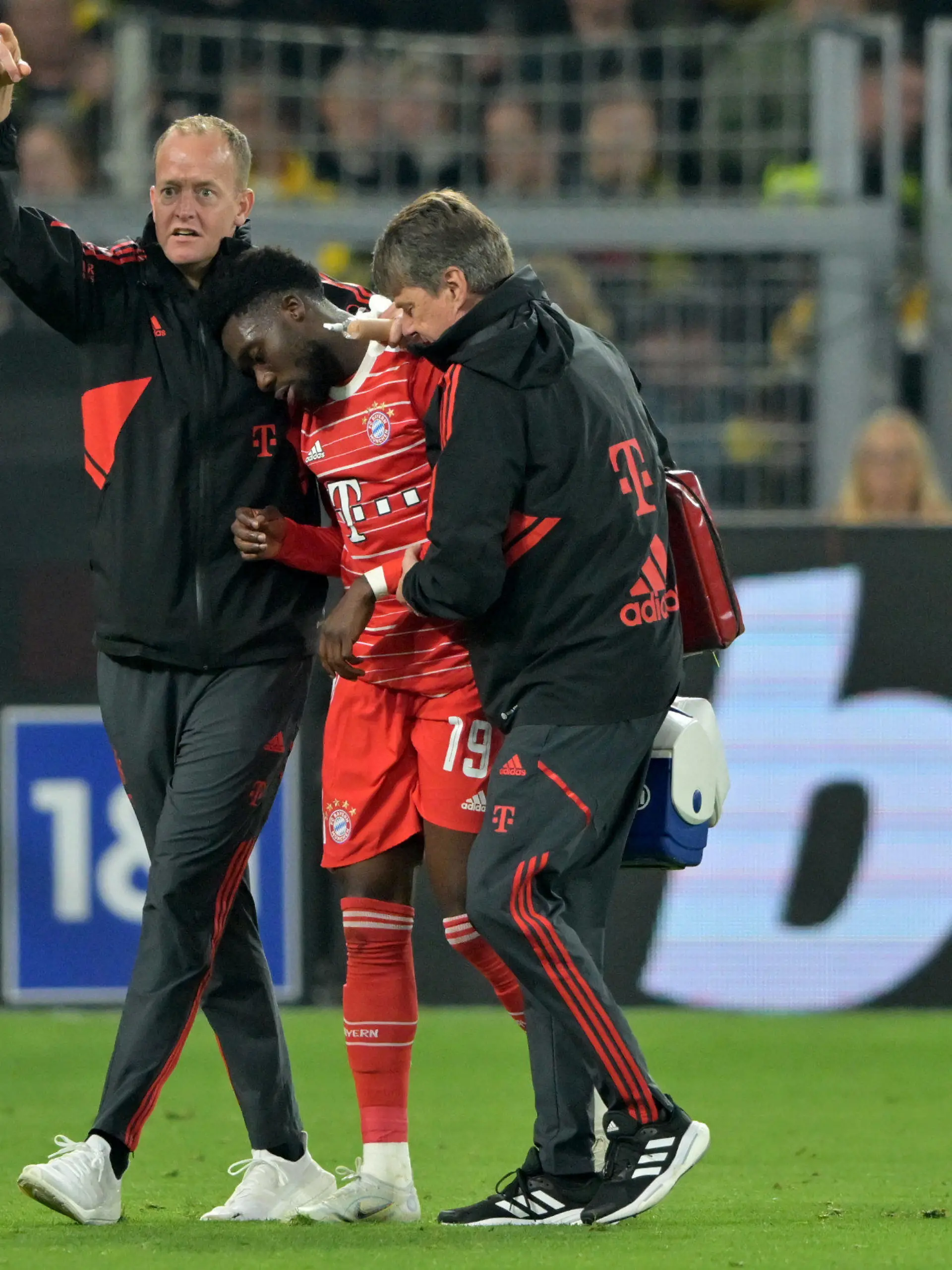 08.10.2022, Nordrhein-Westfalen, Dortmund: Fußball: Bundesliga, Borussia Dortmund - FC Bayern München, 9. Spieltag, Signal Iduna Park. Münchens Alphonso Davies (M) wird nach einer Verletzung vom Platz geführt. WICHTIGER HINWEIS: Gemäß den Vorgaben der DFL Deutsche Fußball Liga bzw. des DFB Deutscher Fußball-Bund ist es untersagt, in dem Stadion und/oder vom Spiel angefertigte Fotoaufnahmen in Form von Sequenzbildern und/oder videoähnlichen Fotostrecken zu verwerten bzw. verwerten zu lassen. Foto: David Inderlied/dpa +++ dpa-Bildfunk +++