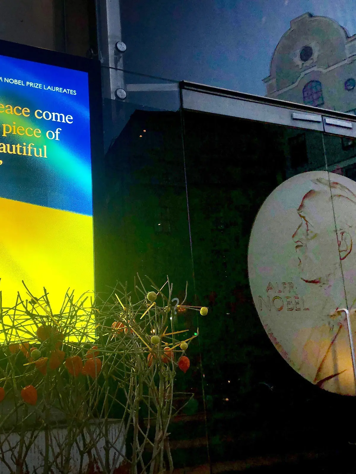 06.10.2022, Schweden, Stockholm: Auf einem Bildschirm vor dem Nobelpreismuseum in Stockholm ist eine Ukraine-Flagge zu sehen mit dem Schriftzug "May peace come to this piece of our beautiful world". Am Vormittag wir der Friedensnobelpreisträger bekannt gegeben. Foto: Steffen Trumpf/dpa +++ dpa-Bildfunk +++
