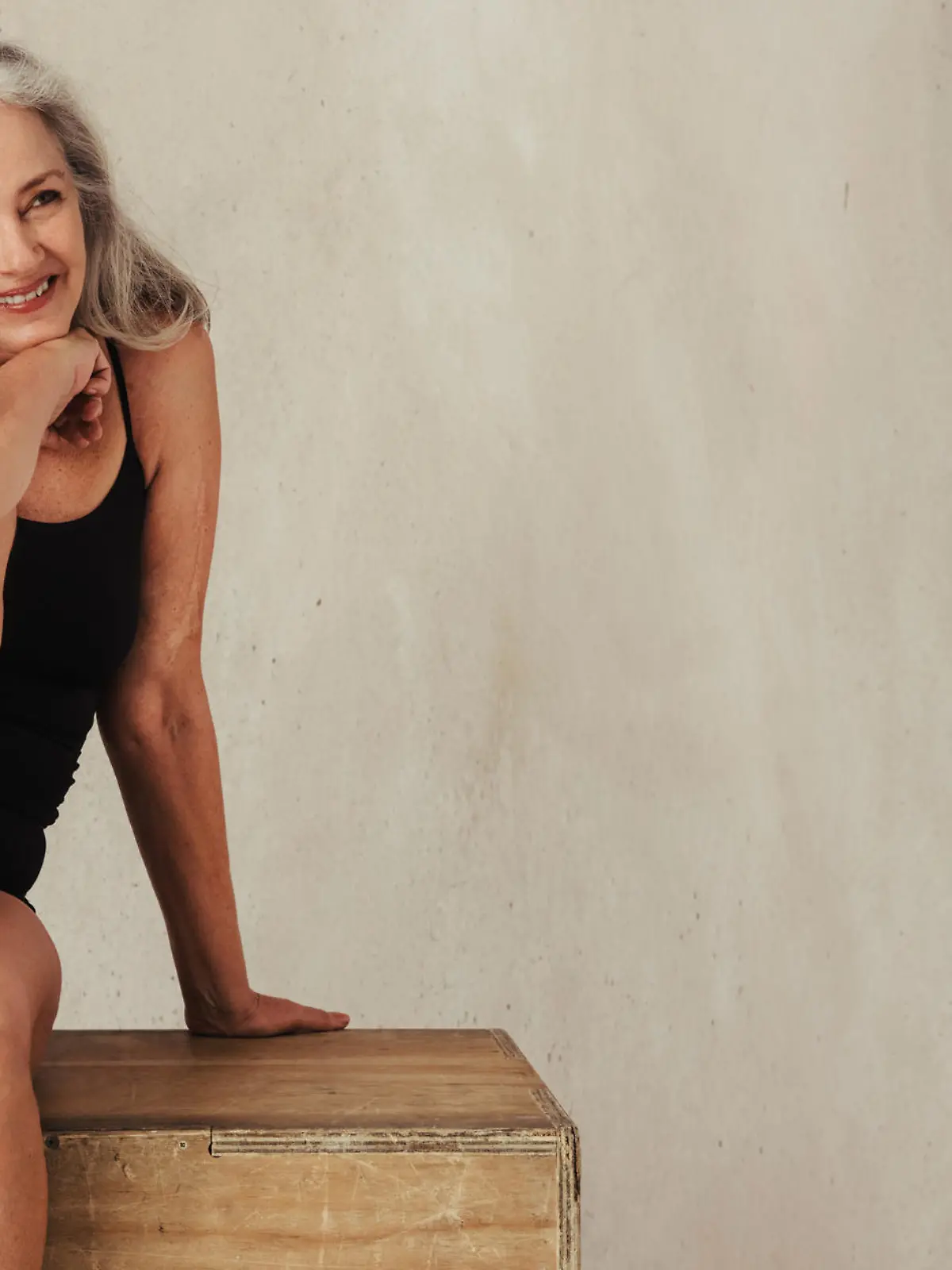 Adult woman smiling while posing in her natural body. Confident woman in black underwear embracing her aging body. Mature woman sitting alone against a studio background.