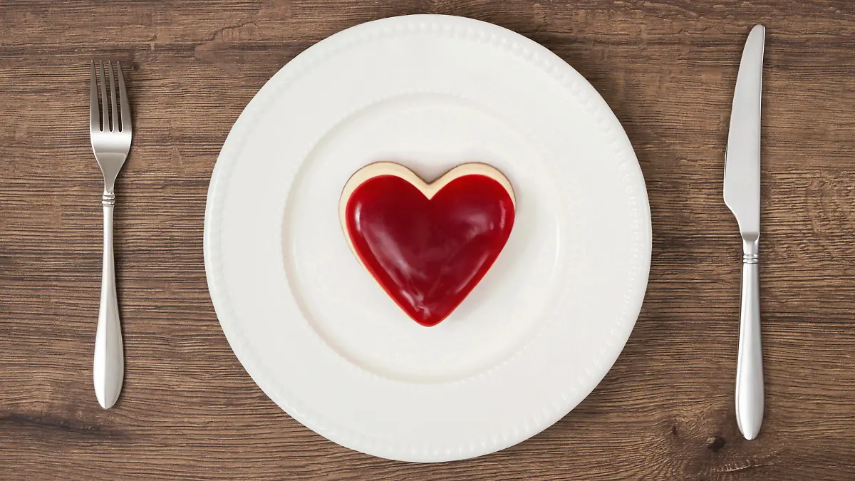 Heart shaped whole mini raspberry cheesecake on red stripe plate with fork and table knife on wooden rustic background.