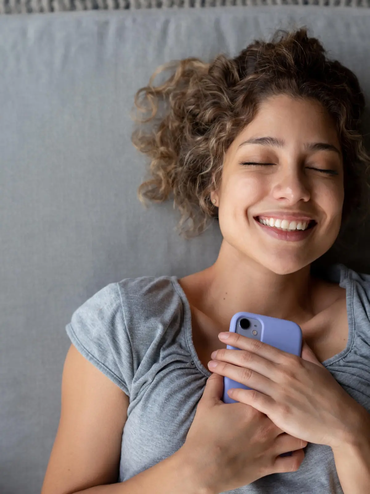Happy woman holding tight to her cell phone while relaxing at home and smiling â technology concepts