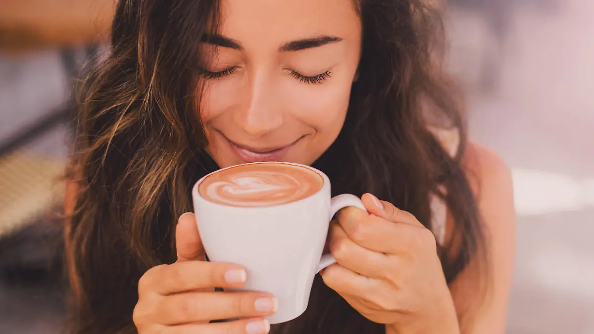Young beautiful happy woman with long curly hair enjoying cappuccino in a street cafe