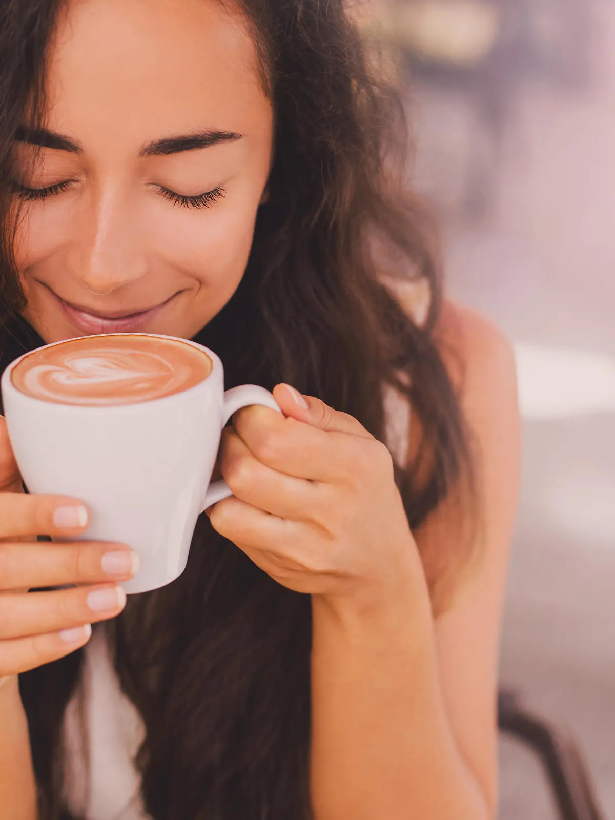 Young beautiful happy woman with long curly hair enjoying cappuccino in a street cafe