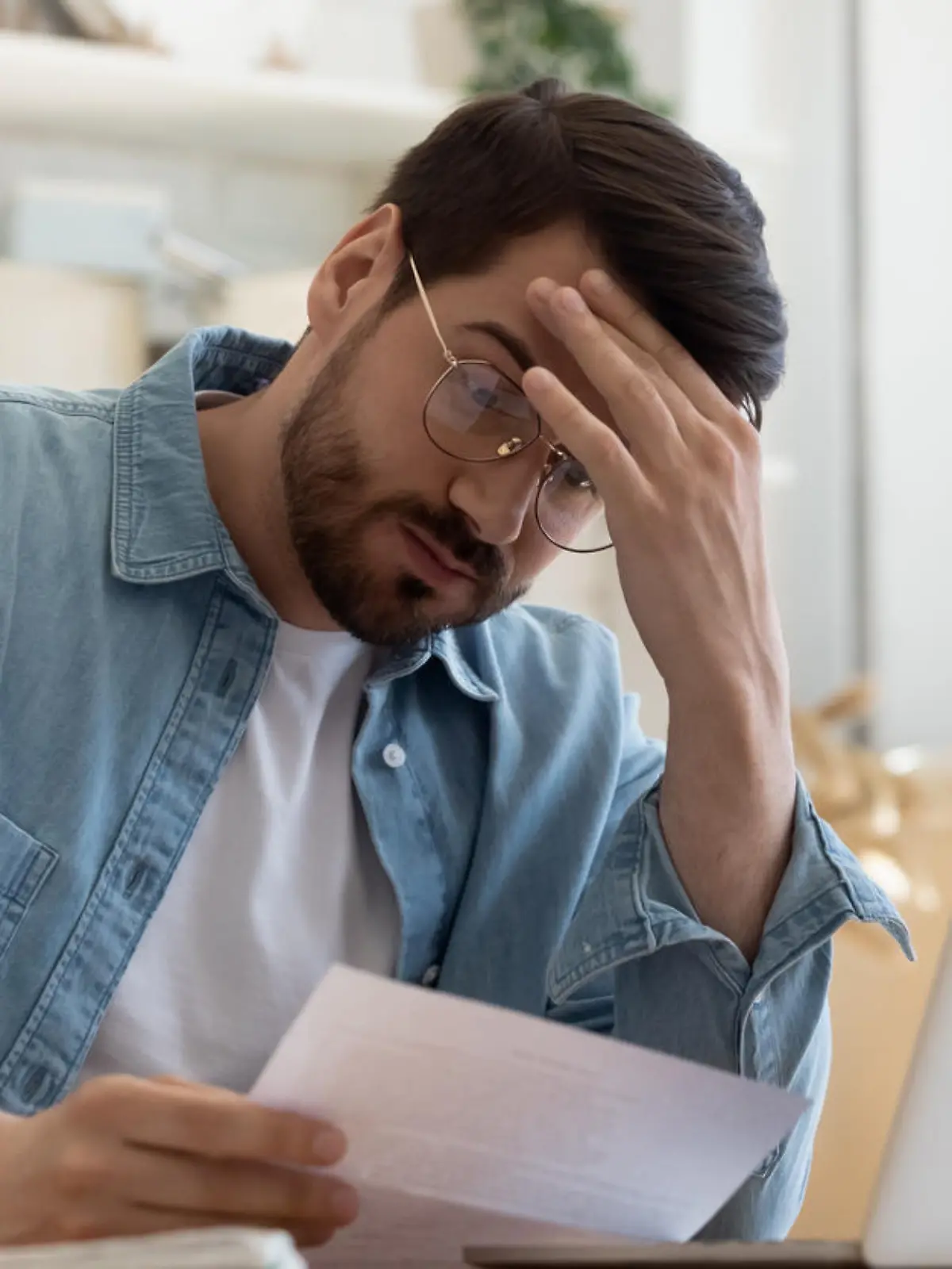 Upset frustrated young man reading bad news in postal mail letter paper document sit at home table, depressed stressed guy worried about high bill tax invoice, overdue debt notification money problem