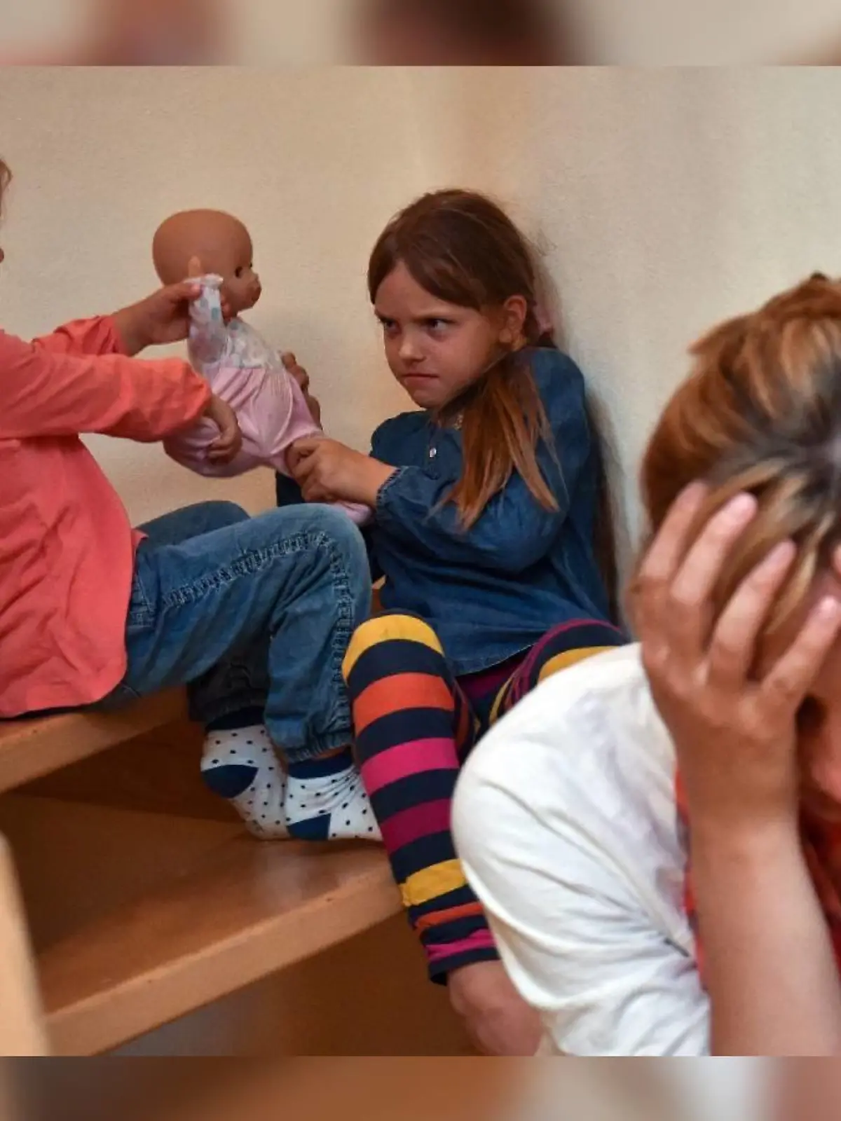 ILLUSTRATION - Gestresst sitzt eine Mutter am 16.06.2014 auf einer Treppe in ihrem Haus in Sieversdorf (Brandenburg), während sich dahinter ihre beiden Kinder um eine Puppe streiten. Die Krankenkasse DAK-Gesundheit stellt am 17.06.2014 eine Studie zu