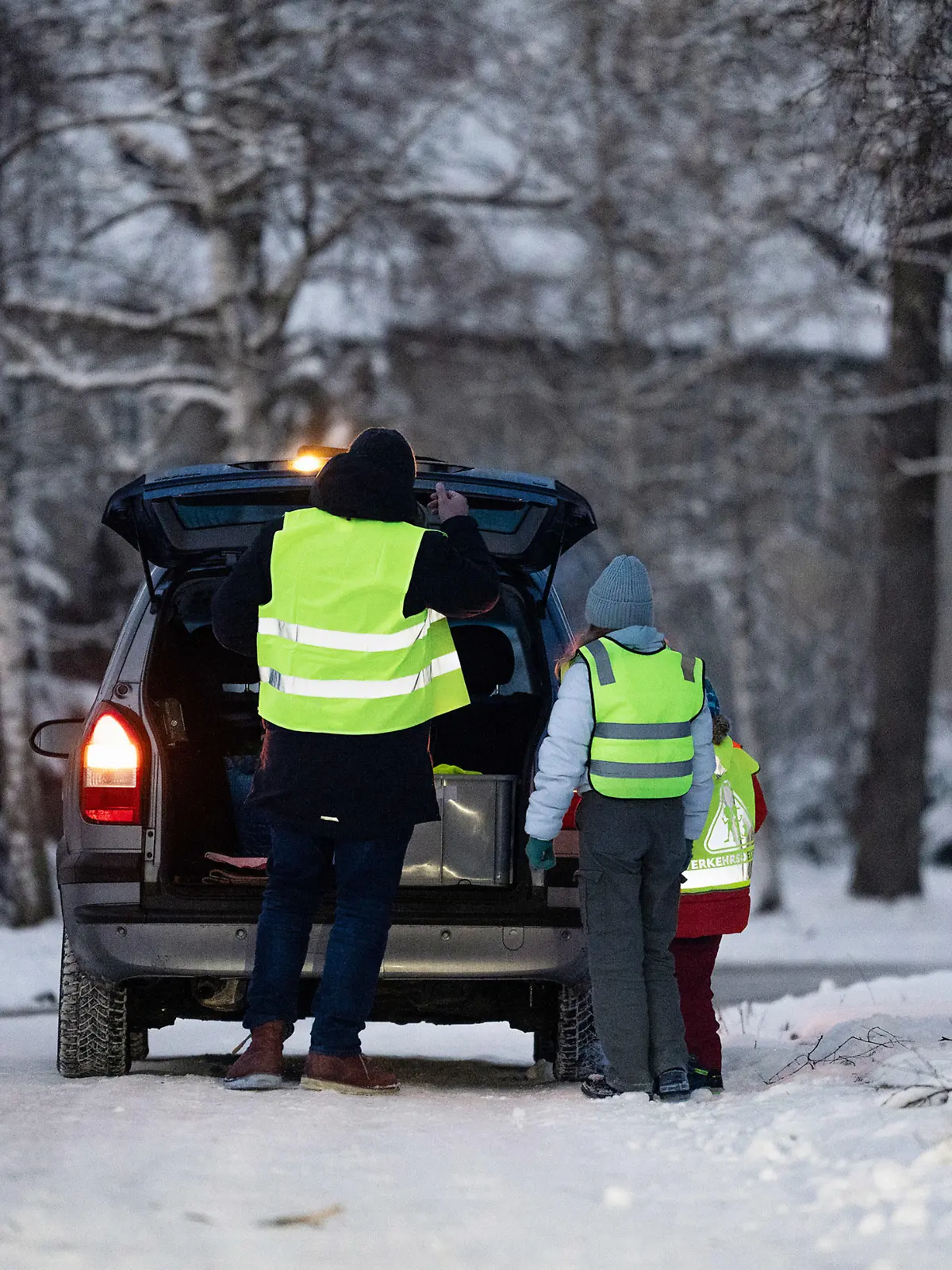 Kind und Elternteil mit Warnweste am Auto