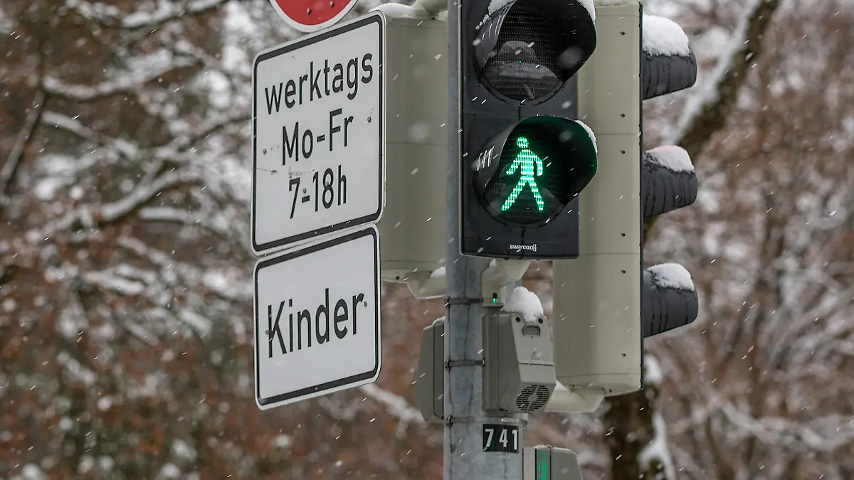 Muenchen, Deutschland 18. Jan 2021: Eine Ampelanlage, auf der das grüne Männchen bei der Fußgängerampel leuchtet. An der Ampel ist das Schild 30 km/h werkstags Mo-Fr. 7-18 h und ein Zusatzschild, auf dem Kinder steht, angebracht