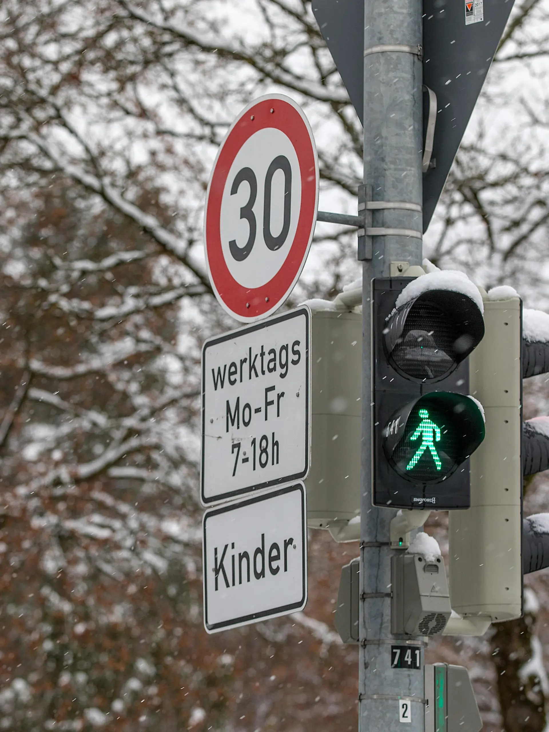 Muenchen, Deutschland 18. Jan 2021: Eine Ampelanlage, auf der das grüne Männchen bei der Fußgängerampel leuchtet. An der Ampel ist das Schild 30 km/h werkstags Mo-Fr. 7-18 h und ein Zusatzschild, auf dem Kinder steht, angebracht