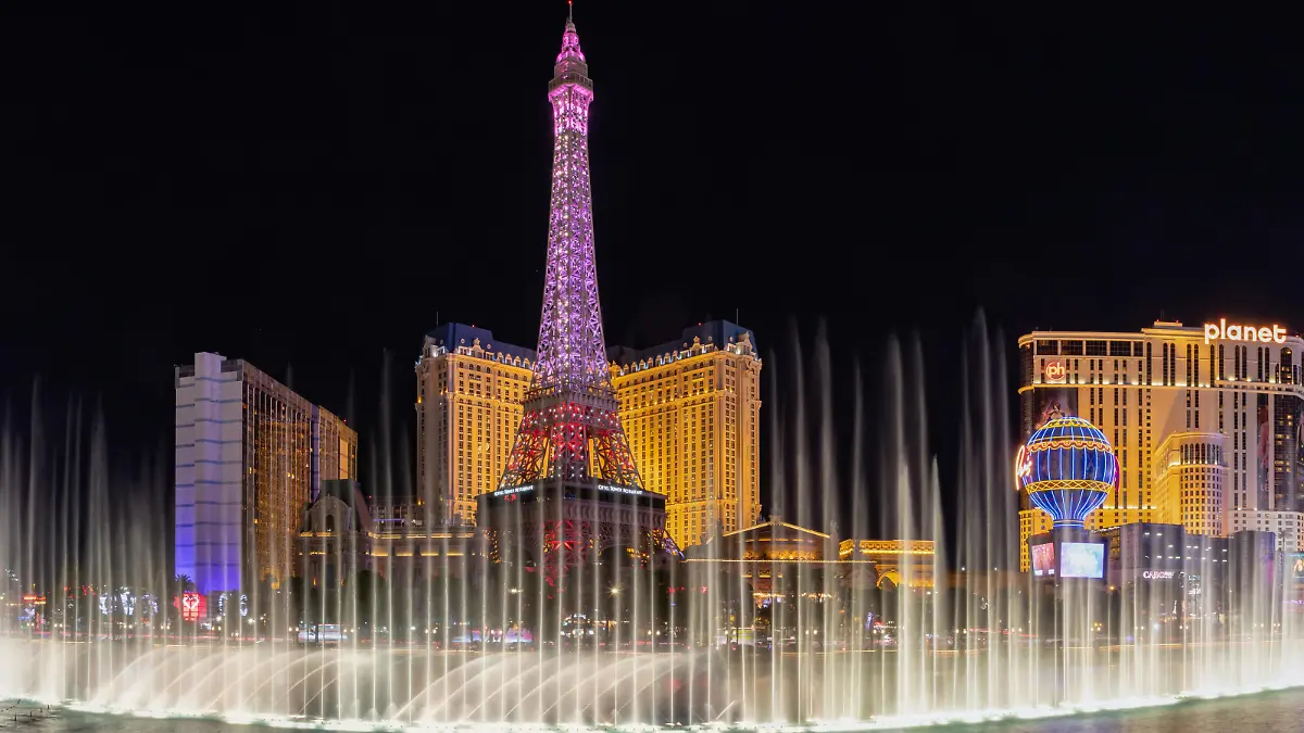 A picture of the Bellagio Fountain Water Show at night, with the Eiffel Tower of the Paris Las Vegas behind it.