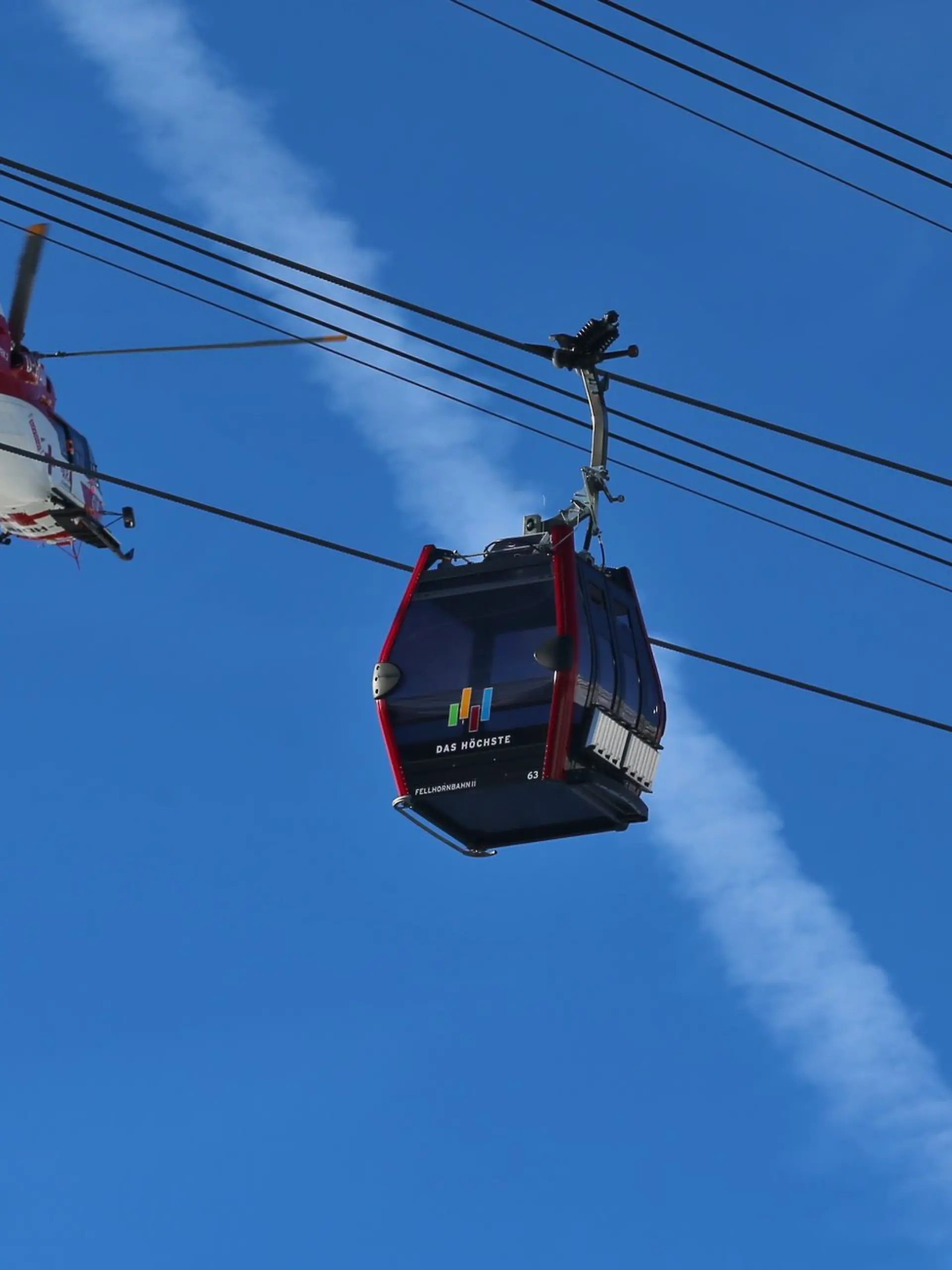 Ein Rettungshubschrauber fliegt nahe der 1780 Meter hoch gelegenen Mittelstation des Fellhorns bei Oberstdorf (Bayern) hinter den Gondeln der Fellhornbahn.
