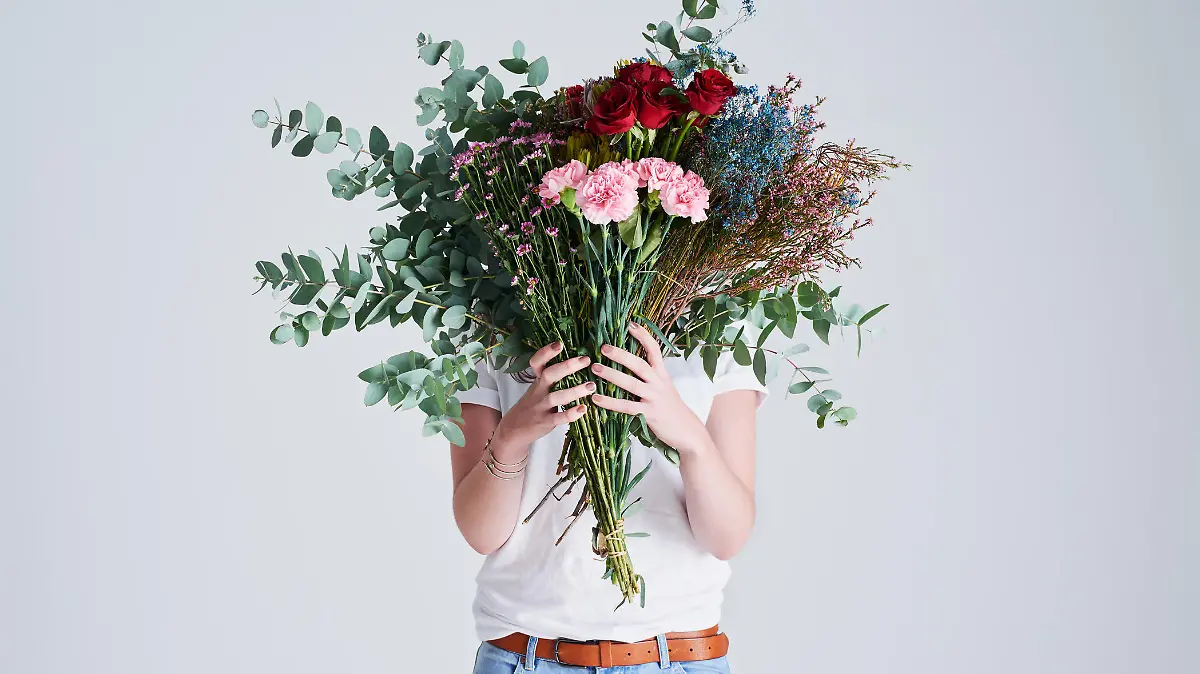 Studio shot of an unrecognizable woman covering her face with flowers against a grey background