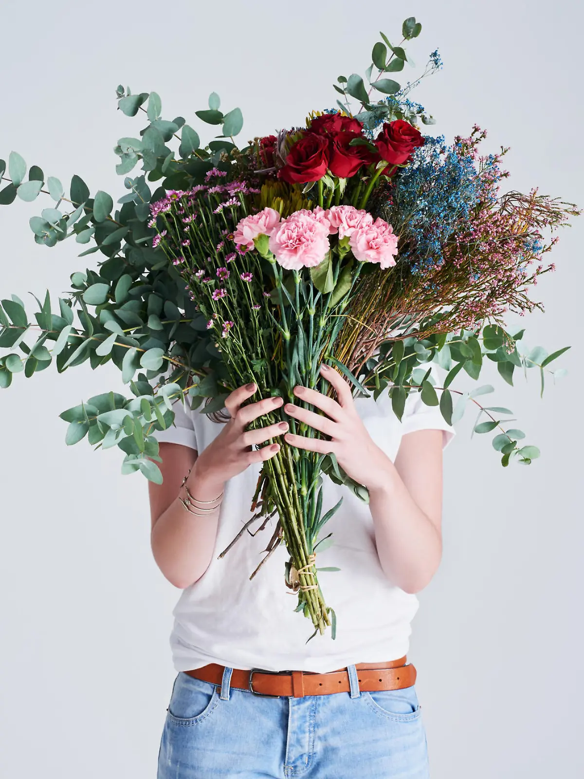 Studio shot of an unrecognizable woman covering her face with flowers against a grey background