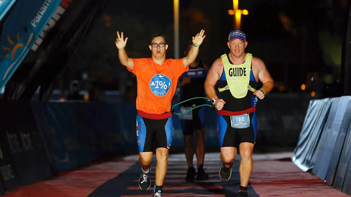 dpatopbilder - HANDOUT - 08.11.2020, USA, Panama City Beach: Mit hochgestreckten Armen läuft Chris Nikoc (l) neben seinem Trainer Dan Grieb beim Ironman 2020 über die Zielline. Nach Angaben der Veranstalter hat der 21 Jahre alte Amerikaner als erster Sportler mit Down-Syndrom einen Ironman absolviert. Für die 3,86 Kilometer Schwimmen, 180,2 Kilometer Radfahren und 42,2 Kilometer Laufen benötigte Chris Nikic beim Ironman Florida inoffiziell 16:46:09 Stunden. Foto: Michael Reaves/Getty Images for IRONMAN/dpa - ACHTUNG: Nur zur redaktionellen Verwendung im Zusammenhang mit der aktuellen Berichterstattung über den Ironman und nur mit vollständiger Nennung des vorstehenden Credits +++ dpa-Bildfunk +++