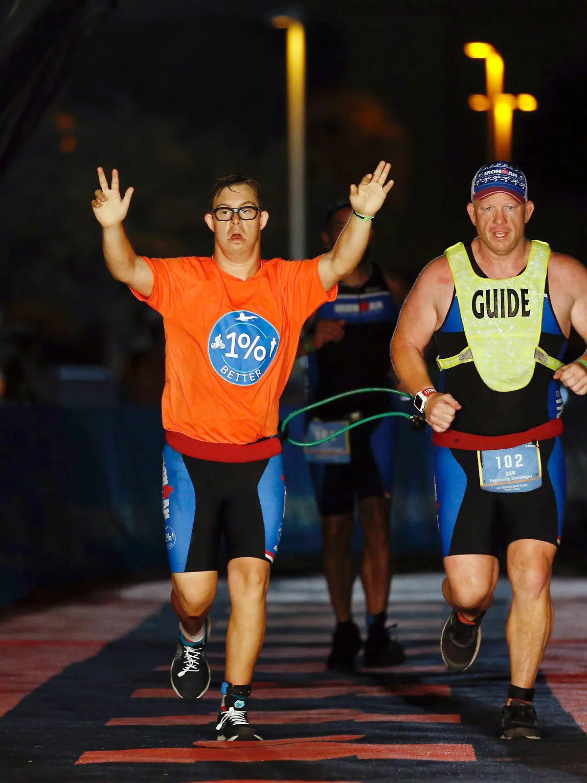 dpatopbilder - HANDOUT - 08.11.2020, USA, Panama City Beach: Mit hochgestreckten Armen läuft Chris Nikoc (l) neben seinem Trainer Dan Grieb beim Ironman 2020 über die Zielline. Nach Angaben der Veranstalter hat der 21 Jahre alte Amerikaner als erster Sportler mit Down-Syndrom einen Ironman absolviert. Für die 3,86 Kilometer Schwimmen, 180,2 Kilometer Radfahren und 42,2 Kilometer Laufen benötigte Chris Nikic beim Ironman Florida inoffiziell 16:46:09 Stunden. Foto: Michael Reaves/Getty Images for IRONMAN/dpa - ACHTUNG: Nur zur redaktionellen Verwendung im Zusammenhang mit der aktuellen Berichterstattung über den Ironman und nur mit vollständiger Nennung des vorstehenden Credits +++ dpa-Bildfunk +++