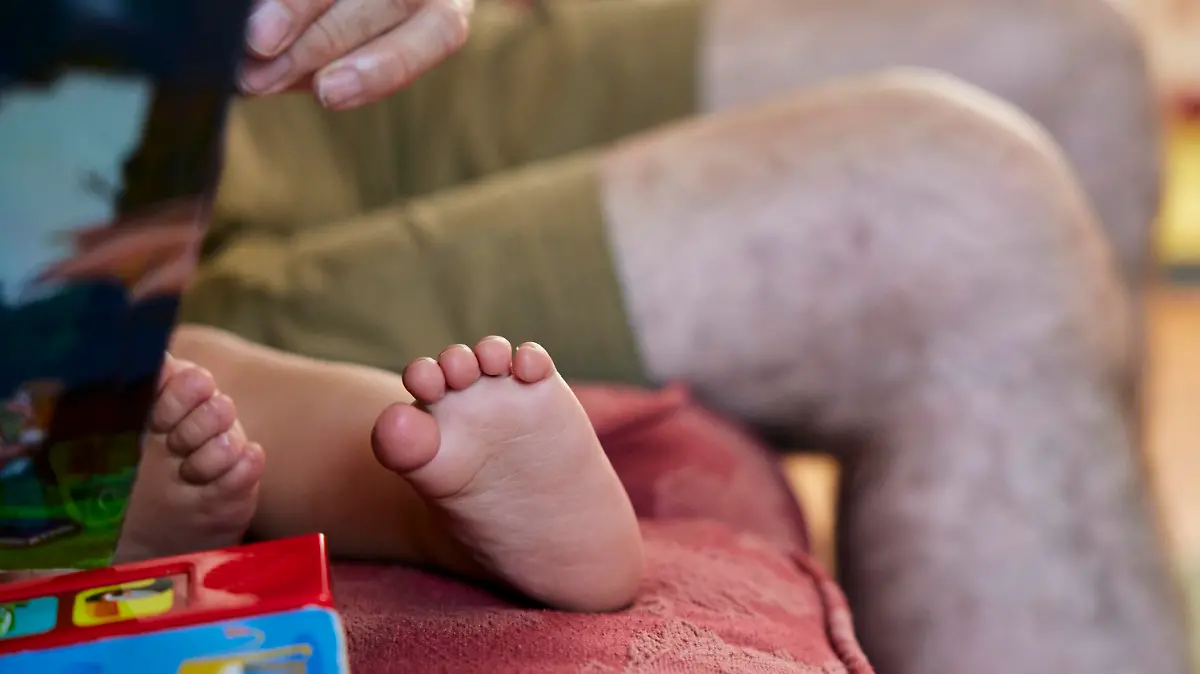 Close up of grandfather reading to toddler, view of the child's bare feet and grandpa's knees. || Modellfreigabe vorhanden / Mindestpreis 20 Euro
