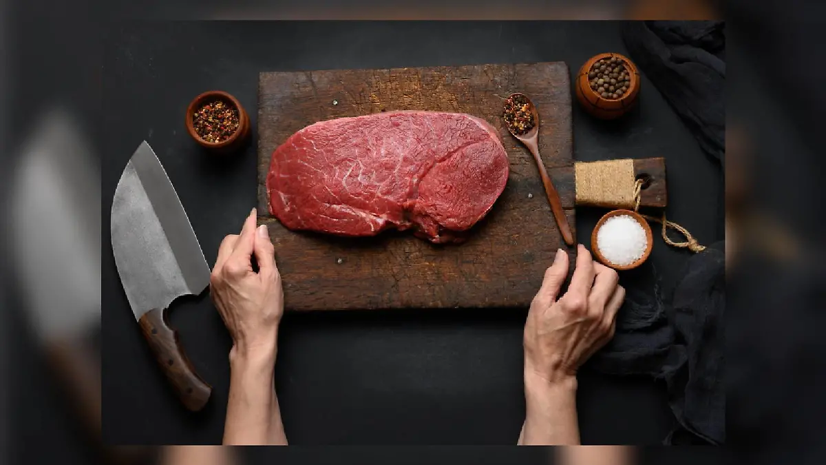 Raw beef tenderloin lies on a wooden cutting board and spices for cooking on a black table, top view and large kitchen knife