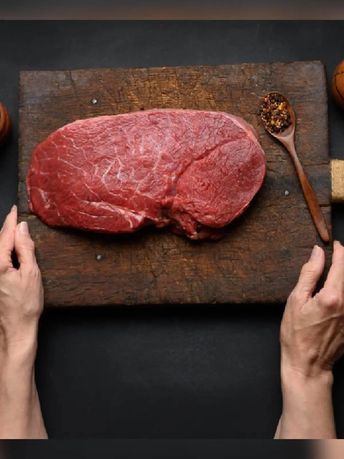 Raw beef tenderloin lies on a wooden cutting board and spices for cooking on a black table, top view and large kitchen knife