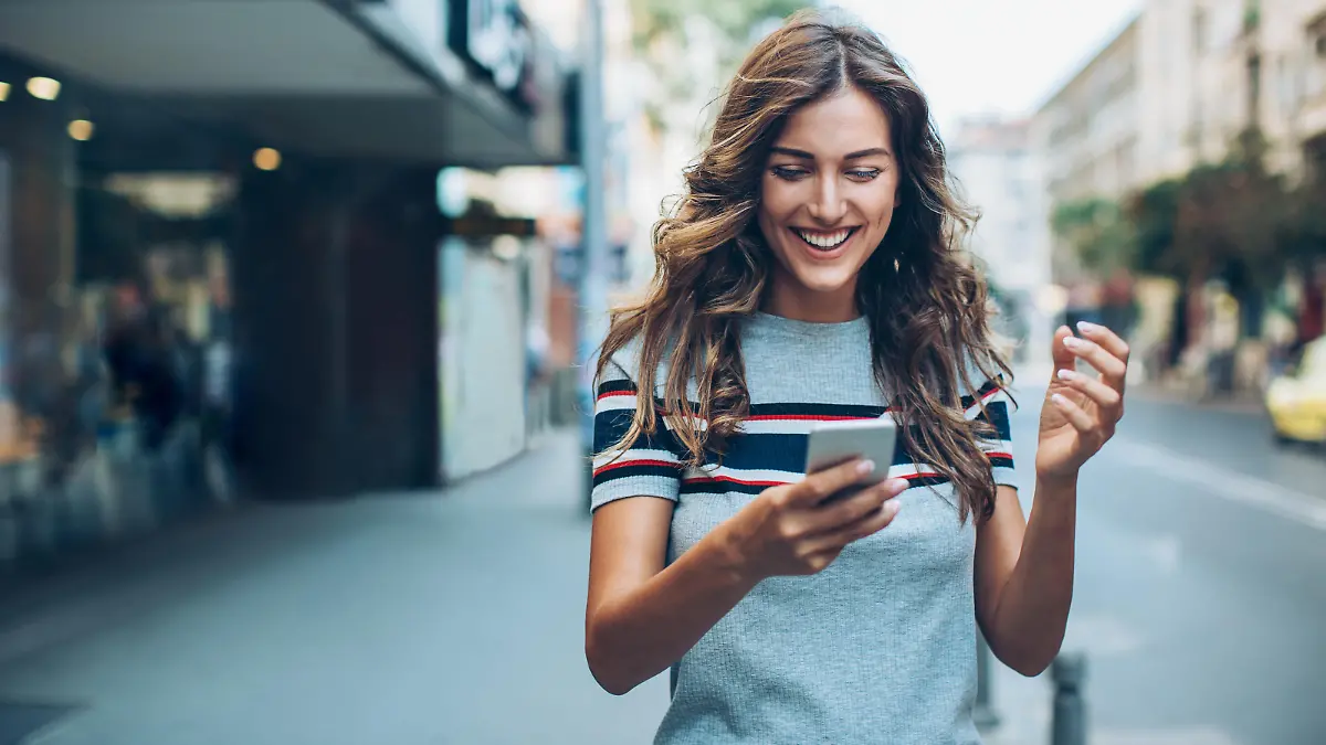 Smiling young woman with smart phone walking on the street, with copy space.