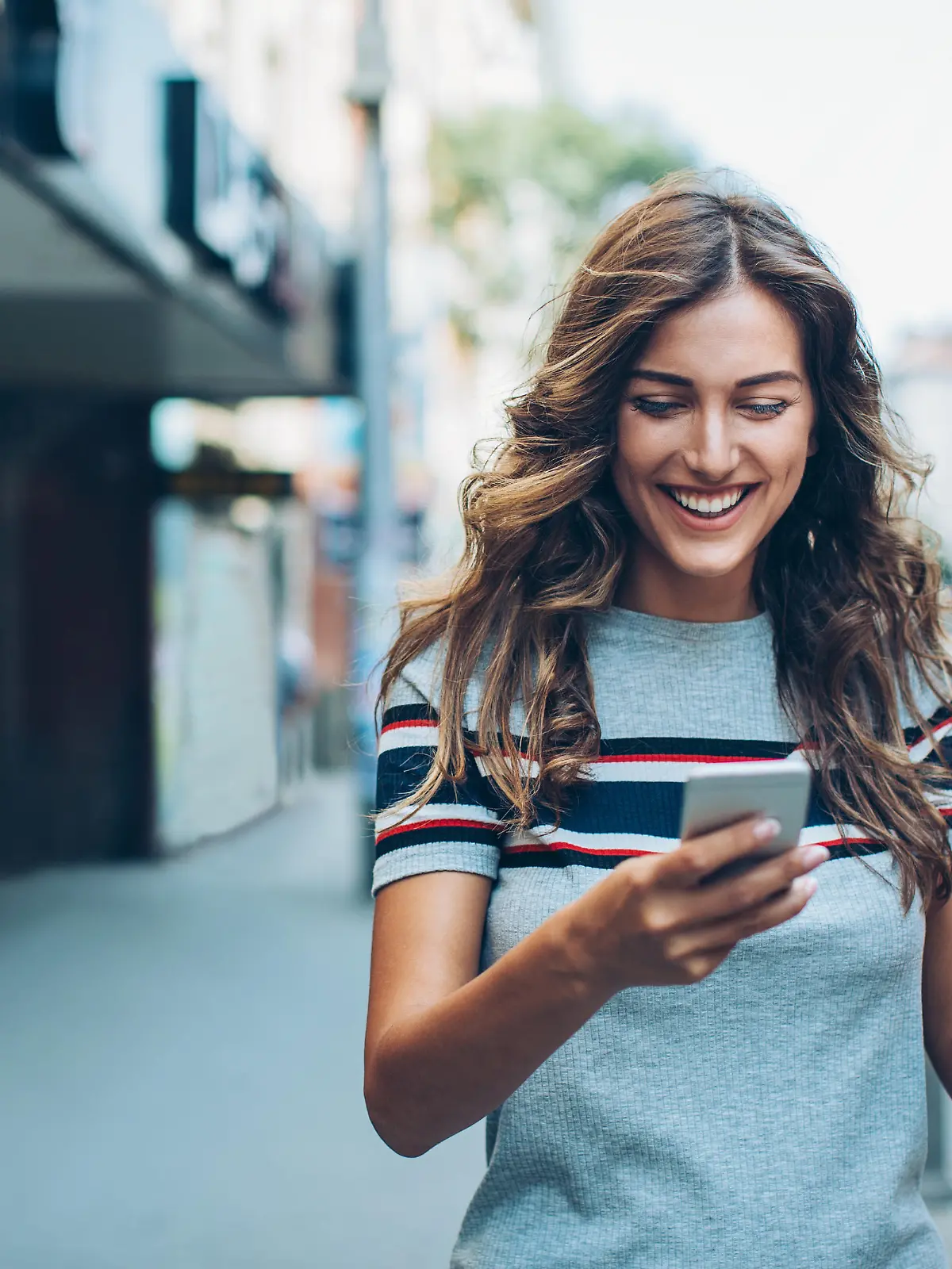 Smiling young woman with smart phone walking on the street, with copy space.