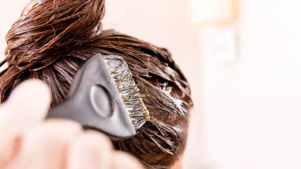 Woman with dying her hair in front of mirror in her own bathroom.