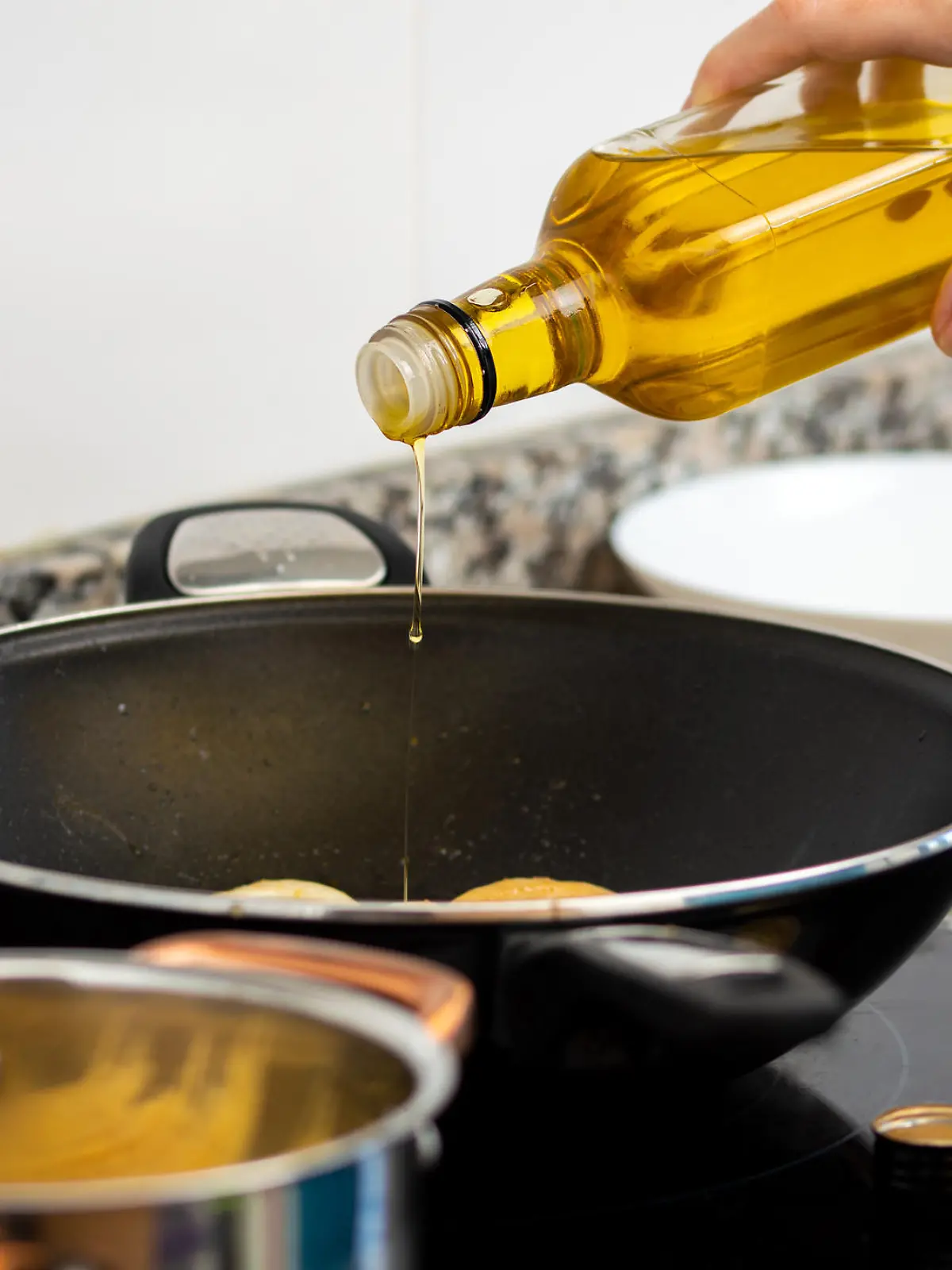 woman pouring cooking oil from bottle into frying pan on stove