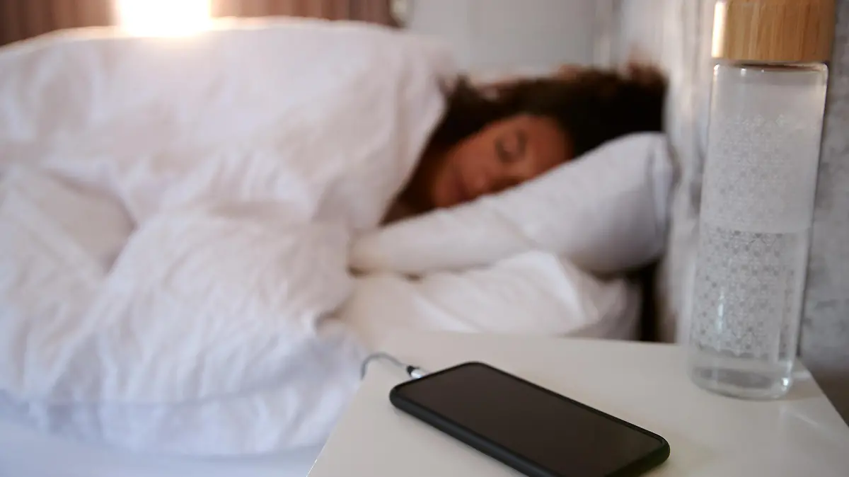 Woman Asleep In Bed With Mobile Phone On Bedside Table