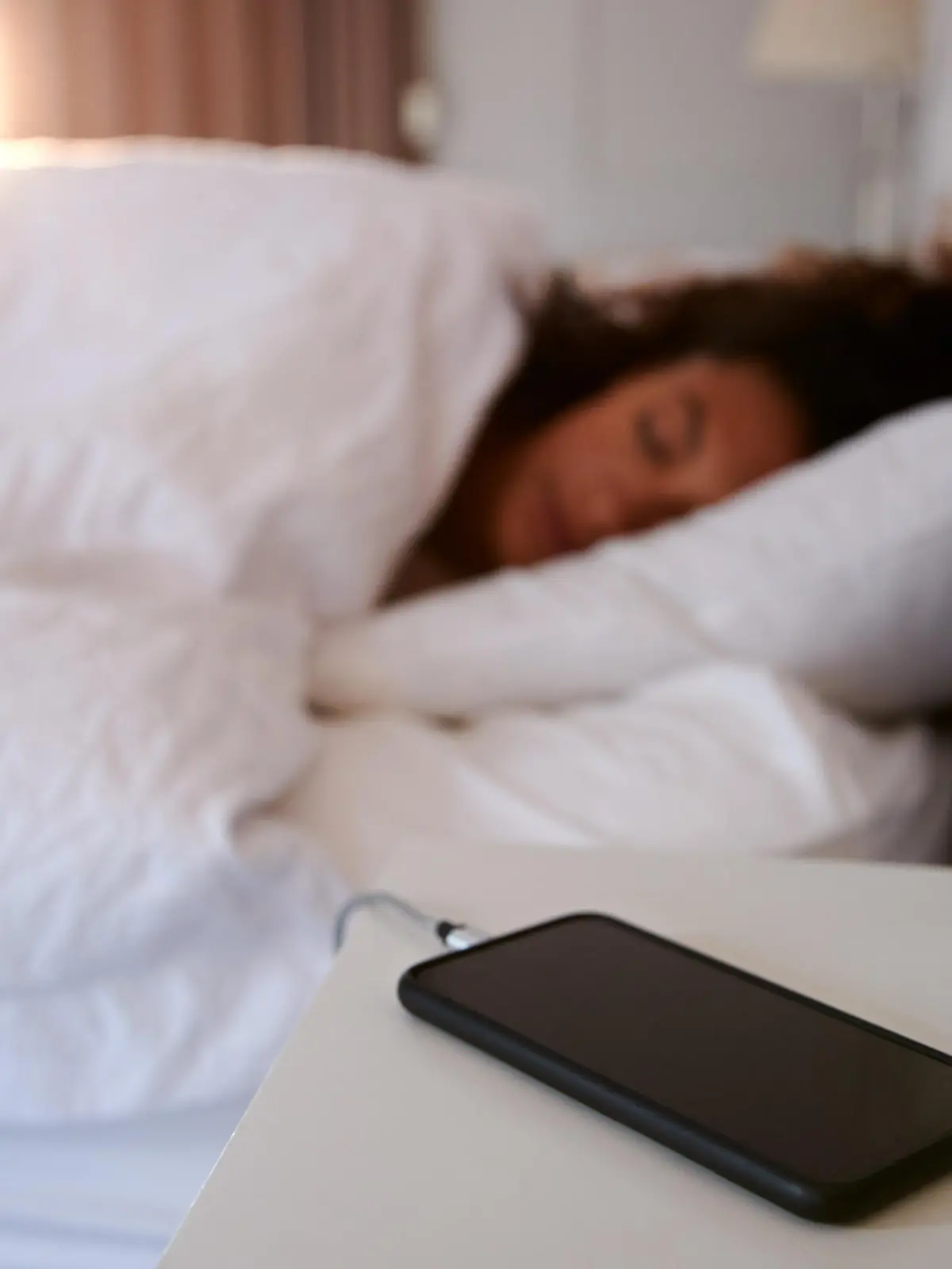 Woman Asleep In Bed With Mobile Phone On Bedside Table