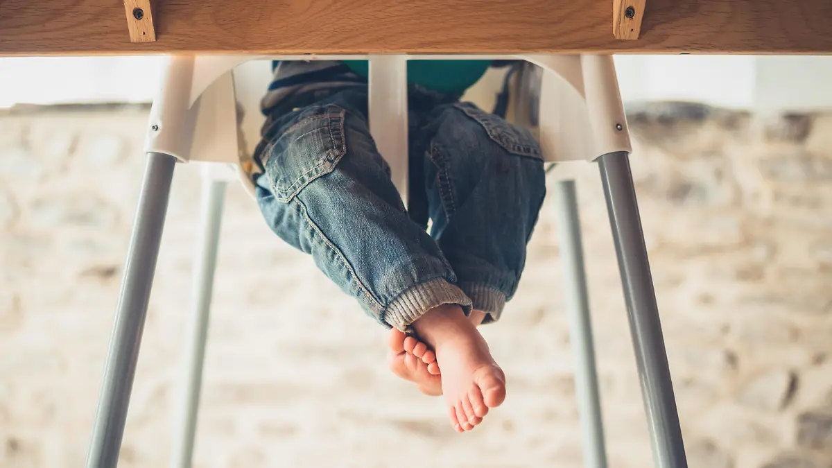 The legs of a little toddler sitting in a high chair at the dining table