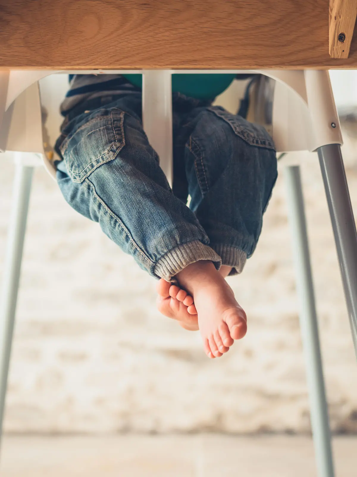 The legs of a little toddler sitting in a high chair at the dining table