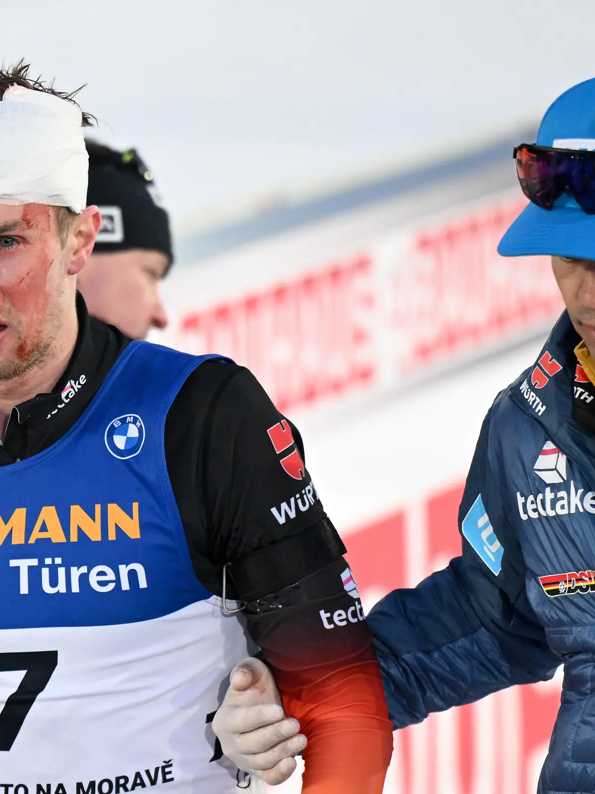 18.02.2024, Tschechien, Nove Mesto Na Morave: Biathlon, Weltmeisterschaft, Massenstart 15 km, Männer. DSV-Arzt Jan Wüstenfeld (r) versorgt im Ziel den am Kopf verletzten Johannes Kühn aus Deutschland. Foto: Hendrik Schmidt/dpa +++ dpa-Bildfunk +++