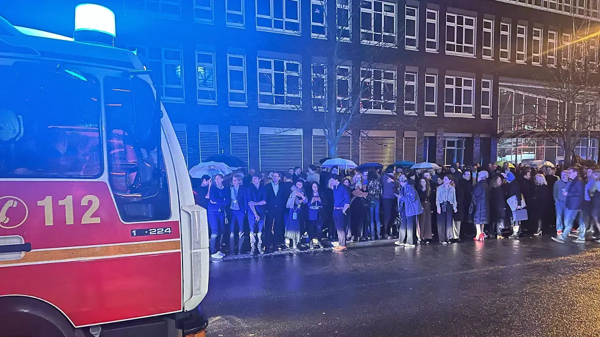 18.02.2024, Berlin: Gäste des NRW-Empfangs im Rahmen der diesjährigen Berlinale stehen hinter einem Feuerwehrwagen auf der Straße und einem Gehweg. Ein Feueralarm hatte die Partygäste am Sonntagabend vor das Gebäude der Landesvertretung in Berlin getrieben. Die 74. Internationalen Filmfestspiele Berlin finden vom 15. bis 25.02.2024 statt. Foto: Thomas Bremser/dpa +++ dpa-Bildfunk +++