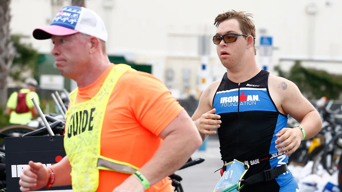 HANDOUT - 07.11.2020, USA, Panama City Beach: Chris Nikic (r) läuft neben seinem Trainer und Guide Dan Grieb, mit dem er mit einem Gurt verbunden ist, beim Ironman 2020. Nach Angaben der Veranstalter hat der 21 Jahre alte Amerikaner als erster Sportler mit Down-Syndrom einen Ironman absolviert. Für die 3,86 Kilometer Schwimmen, 180,2 Kilometer Radfahren und 42,2 Kilometer Laufen benötigte Chris Nikic beim Ironman Florida inoffiziell 16:46:09 Stunden. Foto: Michael Reaves/Getty Images North America/Getty Images for IRONMAN - ACHTUNG: Nur zur redaktionellen Verwendung im Zusammenhang mit der aktuellen Berichterstattung über den Ironman und nur mit vollständiger Nennung des vorstehenden Credits +++ dpa-Bildfunk +++