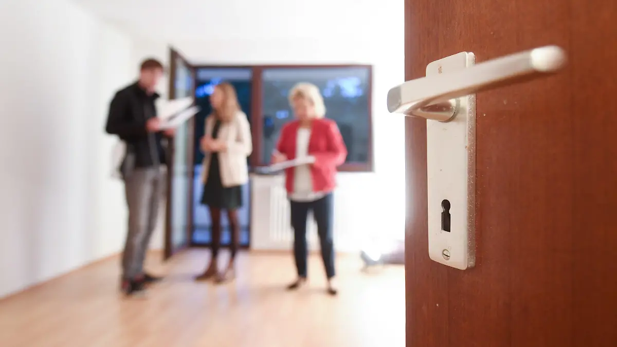 ARCHIV - 19.09.2017, Bayern, München: Eine Maklerin spricht mit Interessenten bei einer Wohnungsbesichtigung während im Vordergrund eine Türklinke zu sehen ist. (zu dpa: «Wohnungsbetrug in Frankfurt: Mittlere zweistellige Zahl an Opfern») Foto: Tobias Hase/dpa +++ dpa-Bildfunk +++
