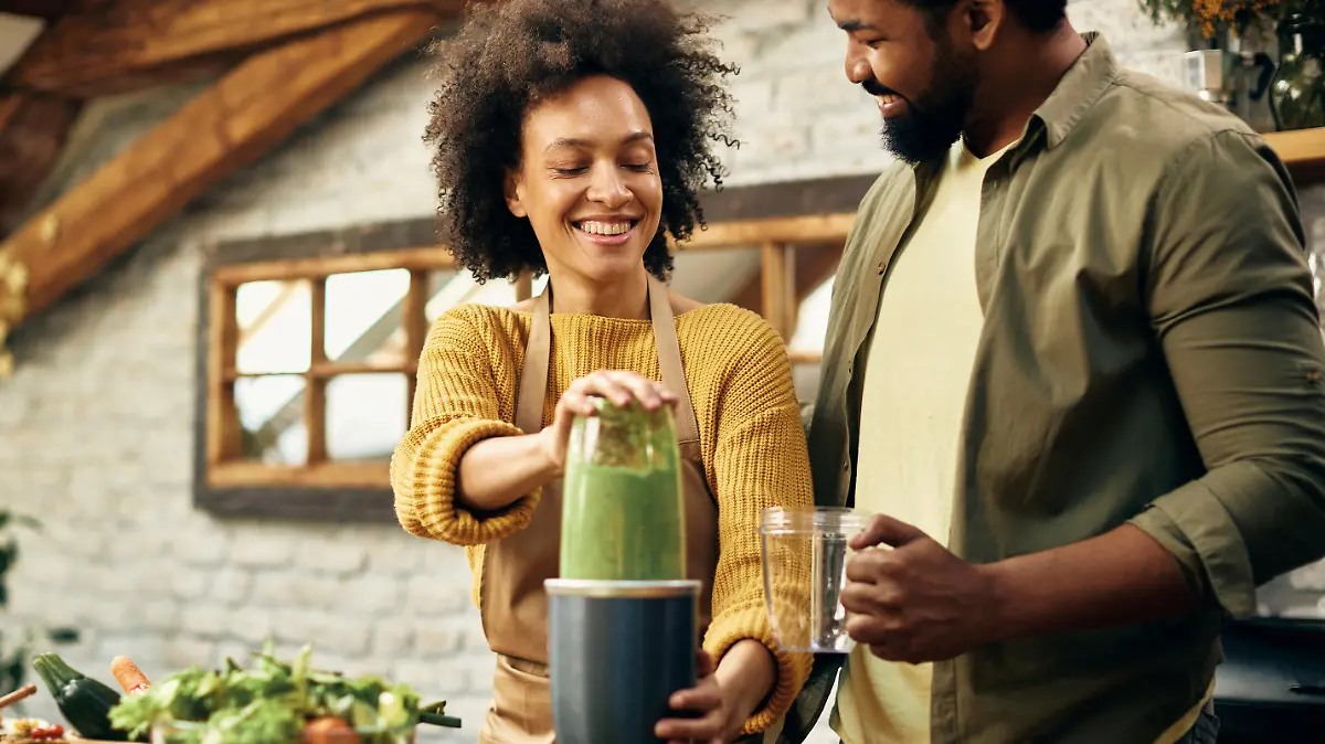 Happy black couple blending fresh vegetables and making smoothie in the kitchen.