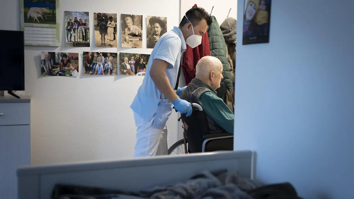 Altenpfleger schiebt einen Rollstuhl im Pflegeheim durch eine Tuer || Modellfreigabe vorhanden