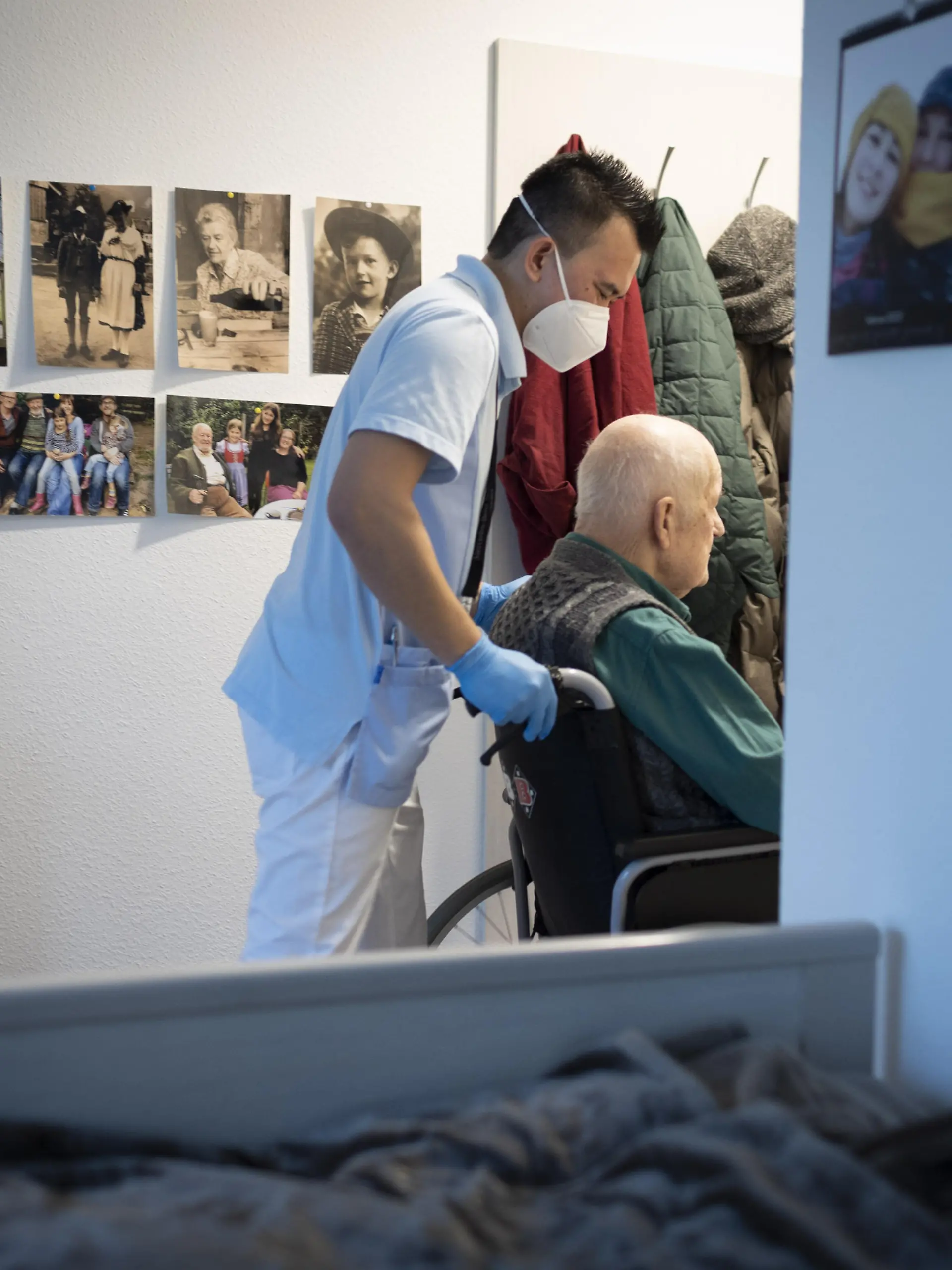 Altenpfleger schiebt einen Rollstuhl im Pflegeheim durch eine Tuer || Modellfreigabe vorhanden