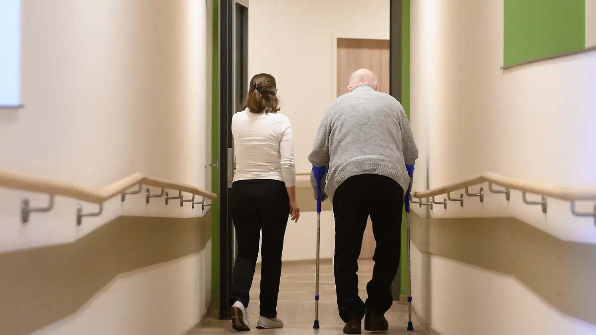 ARCHIV - 22.01.2024, Hessen, Willingen: Ein Patient geht mit Krücken durch einen Flur im Pflegehotel Willingen. Das Pflegehotel Willingen bietet Tagespflege an allen Wochentagen an. (zu dpa: «Hessen will mehr Entlastung in der Pflege schaffen») Foto: Swen Pförtner/dpa +++ dpa-Bildfunk +++