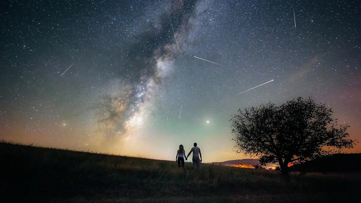 Young man and woman under the bright night sky watching the milky way and Perseid meteor shower