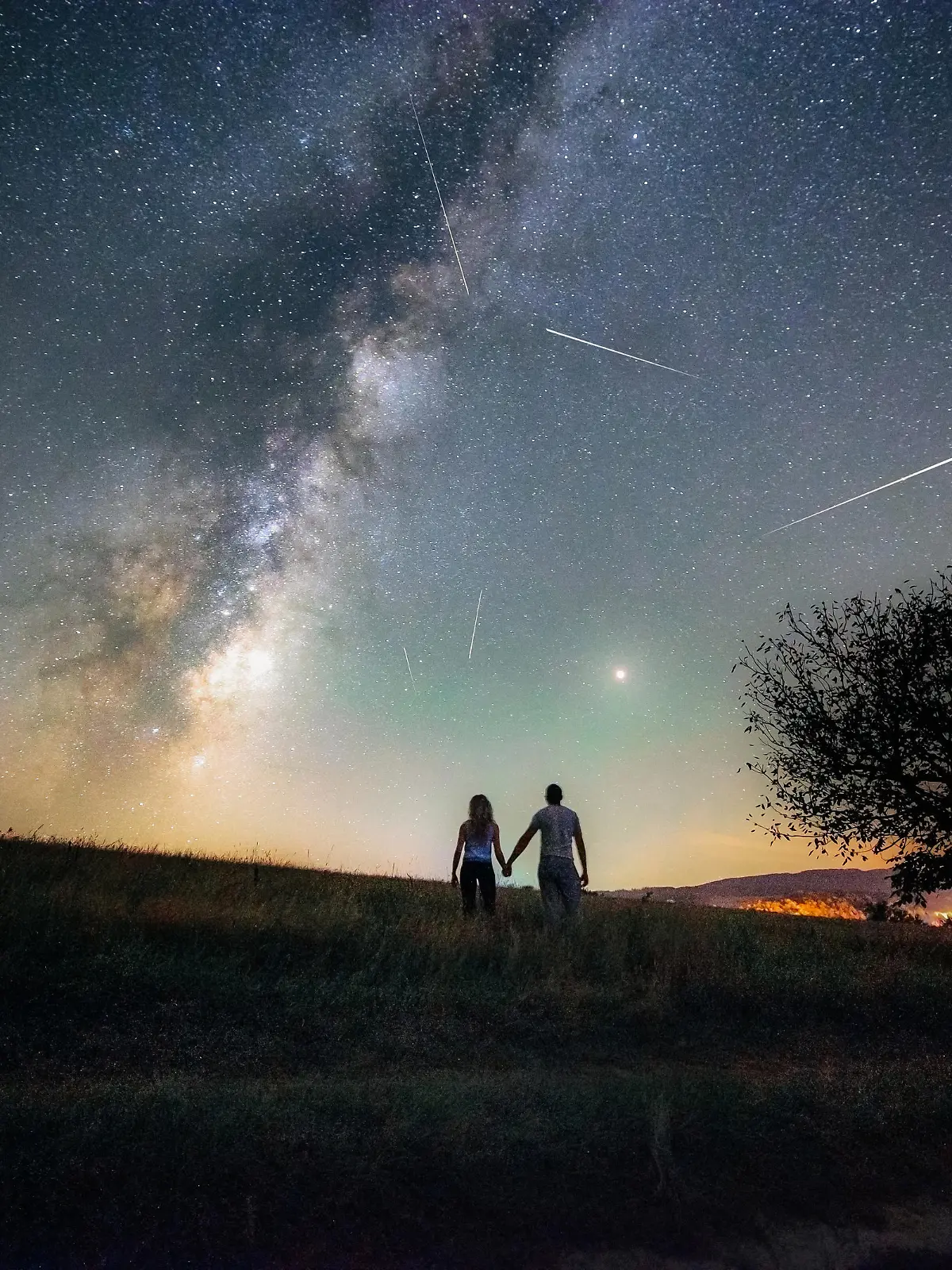 Young man and woman under the bright night sky watching the milky way and Perseid meteor shower