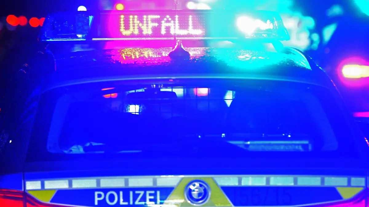 ARCHIV - 18.08.2019, Bayern, Leipheim: Während einer Unfallaufnahme spiegeln sich Blaulicht und der LED-Schriftzug "Unfall" auf dem nassen Dach eines bayerischen Polizeistreifenwagens. (zu dpa: «Drei Menschen bei Unfall auf Bundesstraße 13 schwer verletzt») Foto: Stefan Puchner/dpa +++ dpa-Bildfunk +++