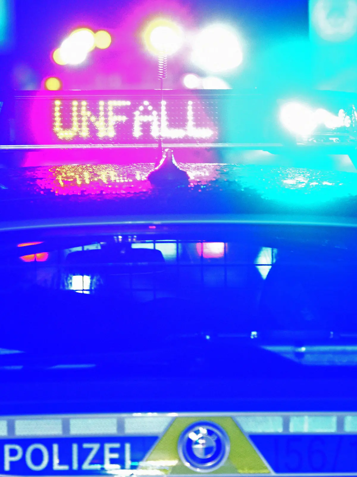 ARCHIV - 18.08.2019, Bayern, Leipheim: Während einer Unfallaufnahme spiegeln sich Blaulicht und der LED-Schriftzug "Unfall" auf dem nassen Dach eines bayerischen Polizeistreifenwagens. (zu dpa: «Drei Menschen bei Unfall auf Bundesstraße 13 schwer verletzt») Foto: Stefan Puchner/dpa +++ dpa-Bildfunk +++