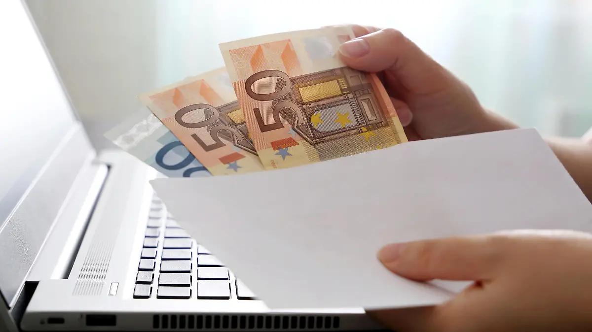 Woman pulls money out of an envelope on laptop background, wages, bonus or bribe concept
