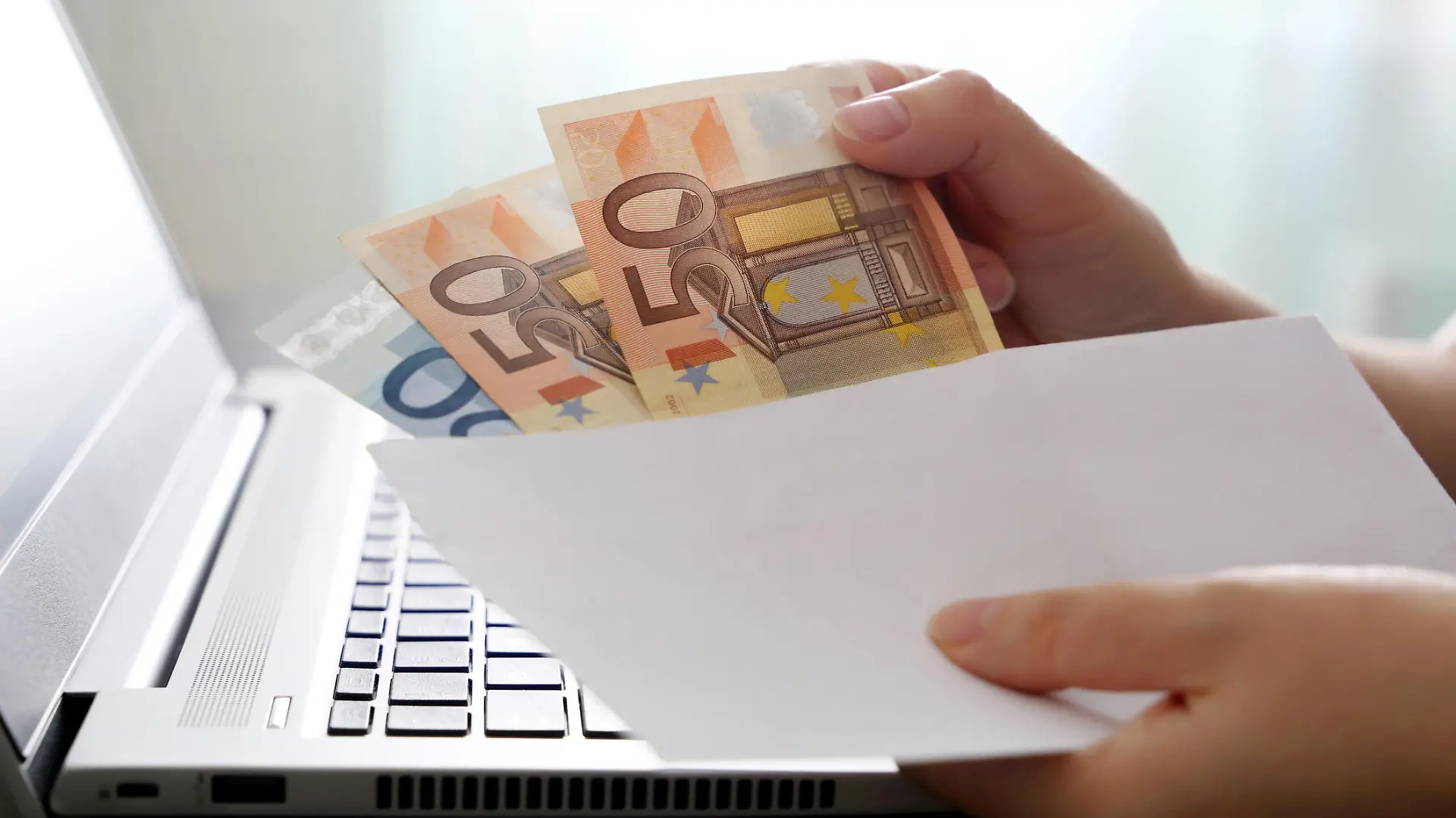 Woman pulls money out of an envelope on laptop background, wages, bonus or bribe concept