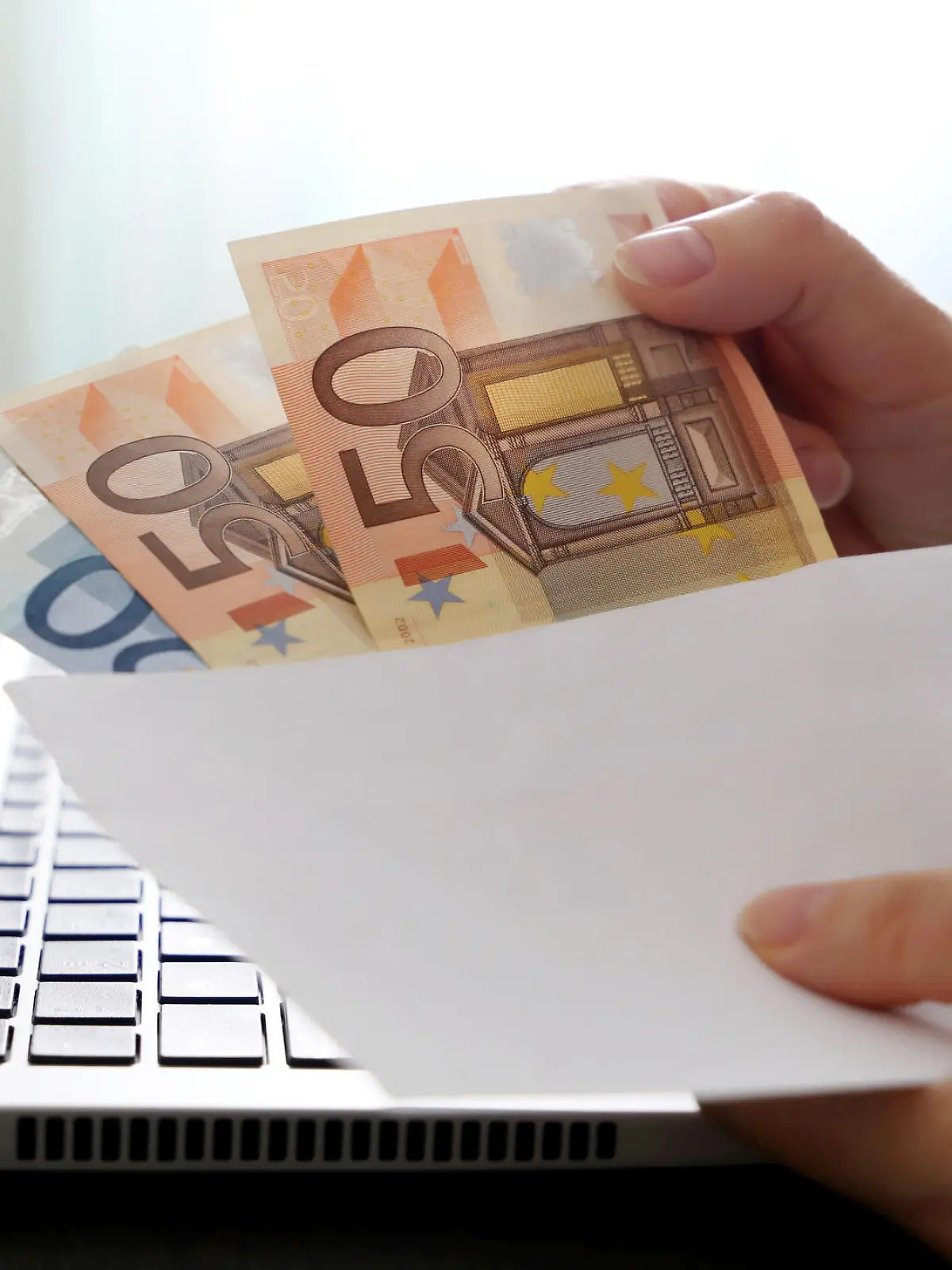 Woman pulls money out of an envelope on laptop background, wages, bonus or bribe concept