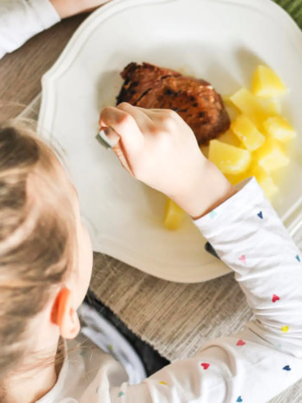 Young girl eating grilled tuna steak and boiled potatoes, Indoors shot of a little girl having a healthy meal decorated with red paprika.