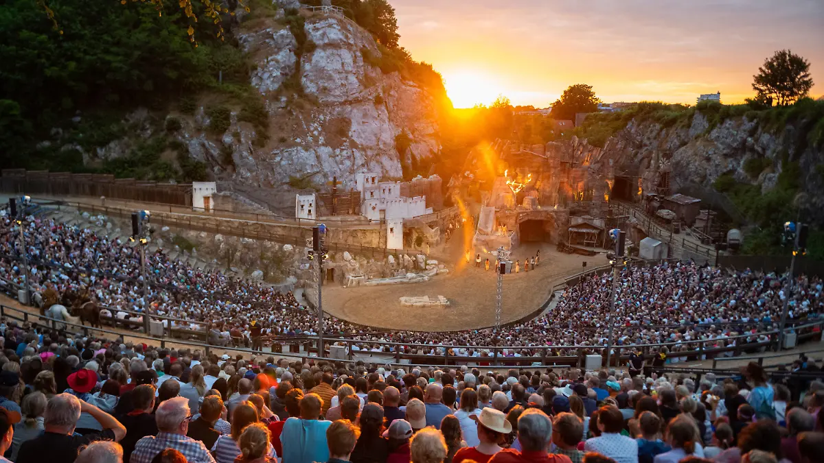 ARCHIV - 24.06.2023, Schleswig-Holstein, Bad Segeberg: Zahlreiche Besucher verfolgen die Aufführung der Premiere  "Winnetou I - Blutsbrüder" der  70. Saison der Karl-May-Spiele in Bad Segeberg vor dem Kalkberg neben der untergehenden Sonne. Seit 1952 werden im Kalkbergstadion von Bad Segeberg Karl Mays Abenteuerromane auf die Bühne gebracht. (zu dpa: «Karl-May-Spiele suchen 35 Komparsen») Foto: Jonas Walzberg/dpa +++ dpa-Bildfunk +++