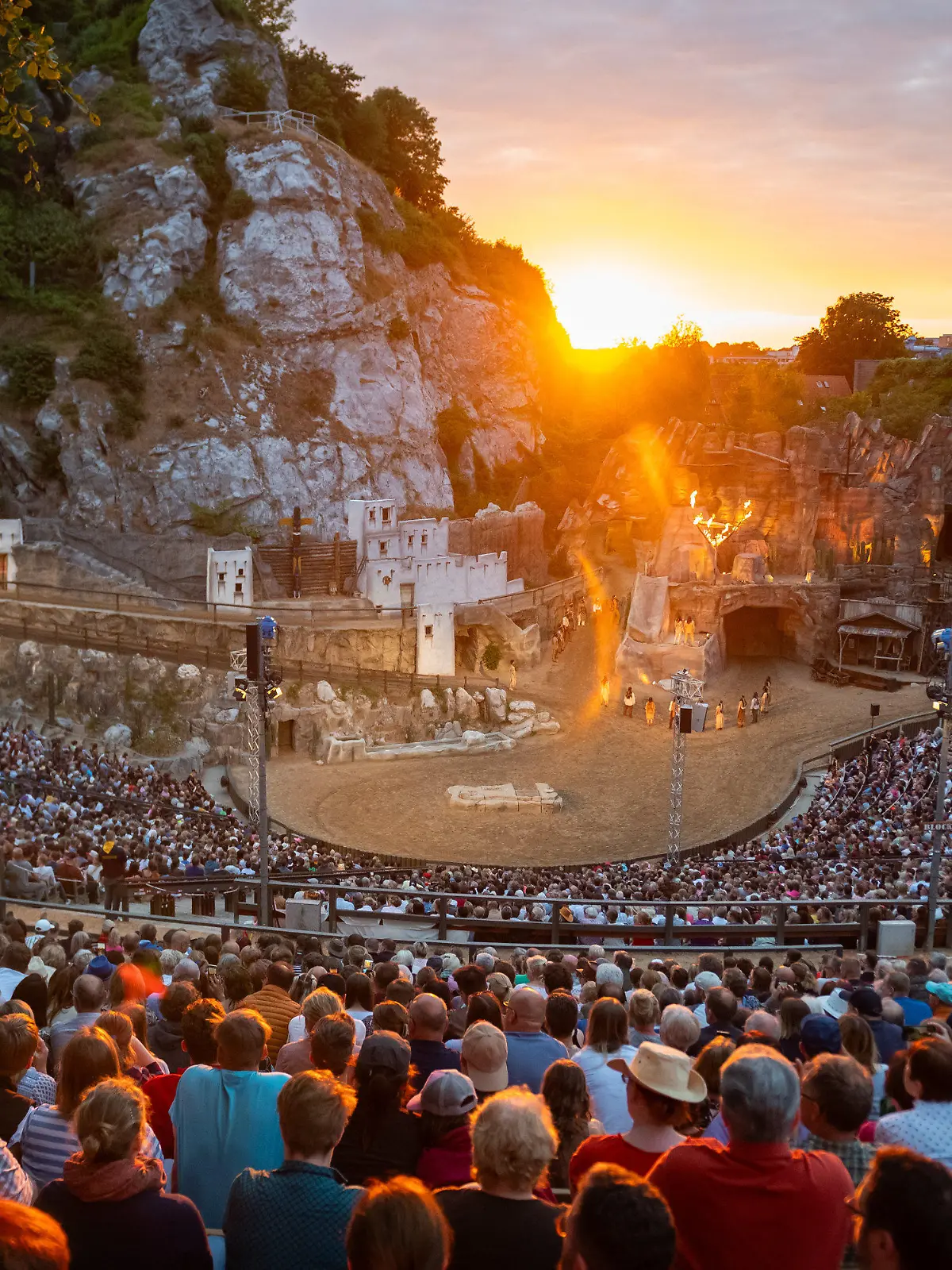 ARCHIV - 24.06.2023, Schleswig-Holstein, Bad Segeberg: Zahlreiche Besucher verfolgen die Aufführung der Premiere  "Winnetou I - Blutsbrüder" der  70. Saison der Karl-May-Spiele in Bad Segeberg vor dem Kalkberg neben der untergehenden Sonne. Seit 1952 werden im Kalkbergstadion von Bad Segeberg Karl Mays Abenteuerromane auf die Bühne gebracht. (zu dpa: «Karl-May-Spiele suchen 35 Komparsen») Foto: Jonas Walzberg/dpa +++ dpa-Bildfunk +++